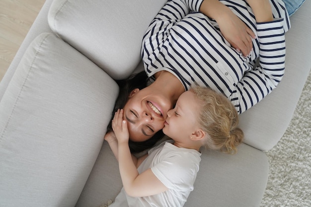 Mãe feliz descansando com sua filha no sofá. Família brincando e relaxando juntos. Mulher e criança estão sorrindo e adormecendo juntos. Caucasiana mãe e filho dormindo durante o dia.