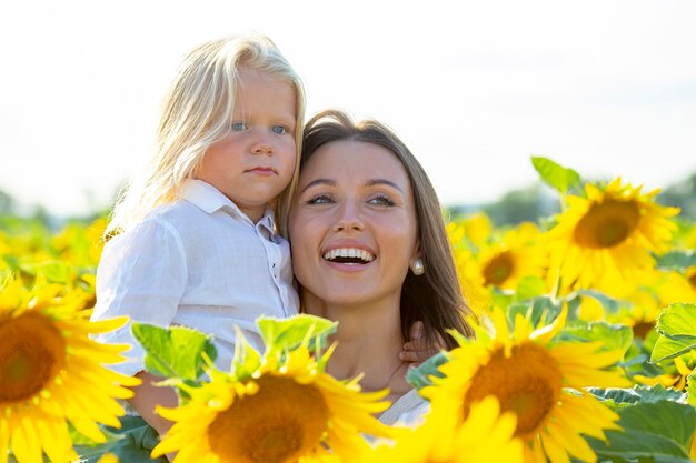 Mãe feliz e adorável filho loiro juntos perto de um campo de girassóis sob a luz do sol