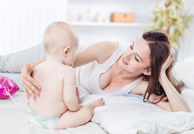 Mãe feliz e bebê de ano na cama no quarto