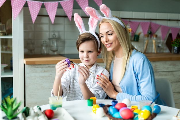 Mãe feliz e bonito filho pintar ovos de Páscoa juntos. Conceito de Páscoa