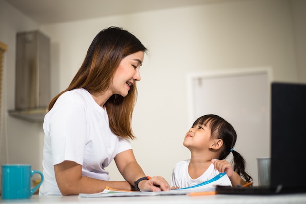 Mãe feliz e filha sorridente juntos pintando com marcadores. Mãe ajudando criança adotada com a lição de arte. Mãe alegre e menina asiática fazendo pintura em casa.