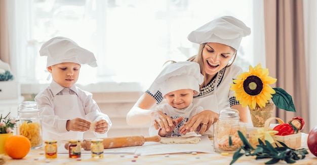 Mãe feliz e seus filhos fazem biscoitos na cozinha