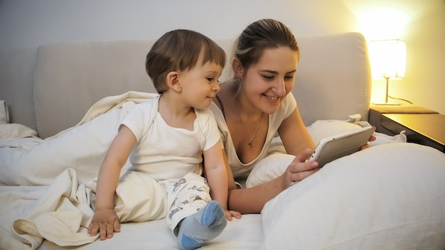 Mãe feliz e sorridente com o filho da criança assistindo vídeo no tablet à noite.