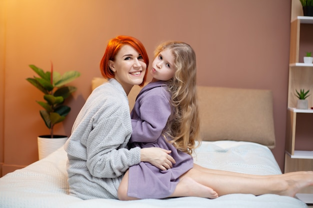 Mãe feliz e sua filha bebê na cama no quarto