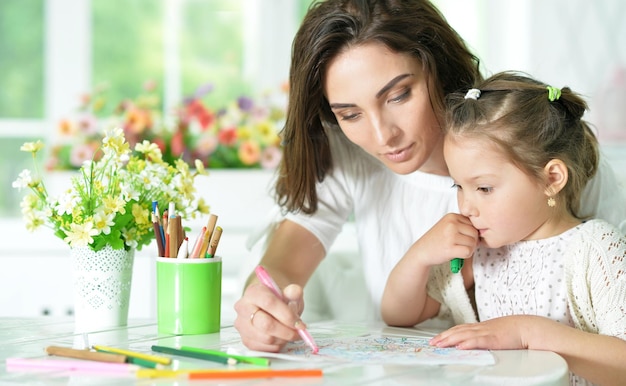 Mãe feliz e sua filhinha desenhando com lápis juntas