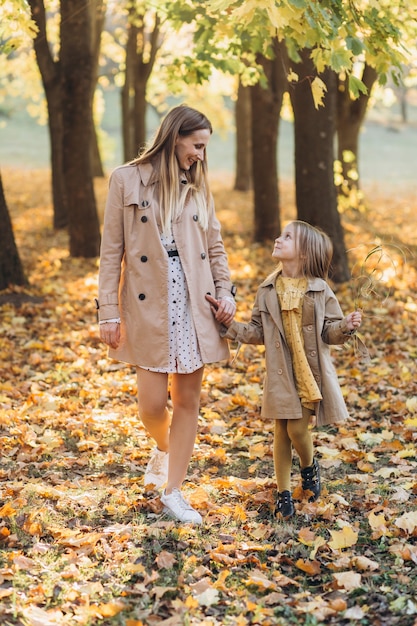 Mãe feliz e sua linda filha se divertem e caminham no parque outono.