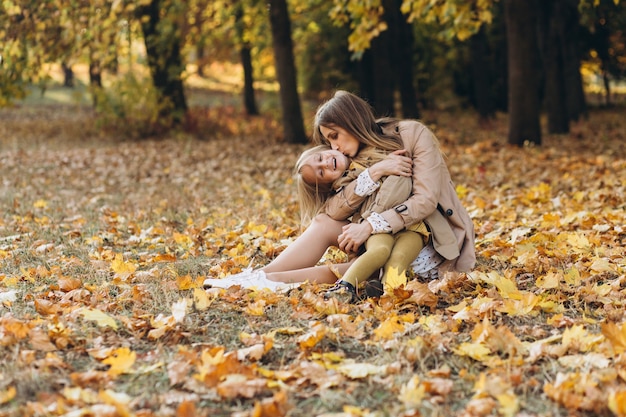 Mãe feliz e sua linda filha sentada e se divertindo entre as folhas amarelas no parque outono.