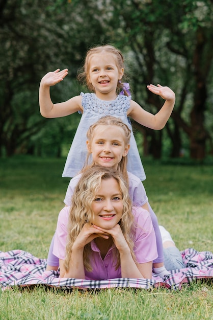 Mãe feliz e suas filhas relaxam no parque no verão, sentadas em um cobertor