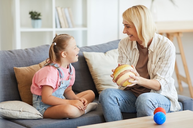 Mãe feliz mostrando o modelo dos planetas para sua filha com síndrome de down e elas rindo sentadas no sofá em casa