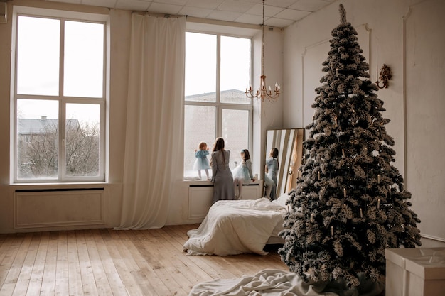 Mãe festiva com varas de pescar em pé na janela da sala com uma árvore de natal