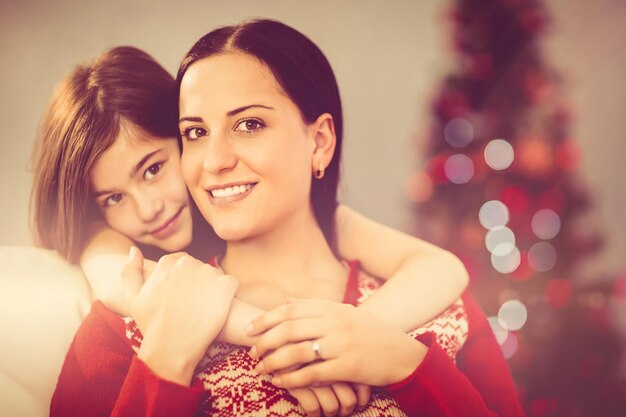 Foto mãe festiva e filha sorrindo para a câmera em casa na sala de estar