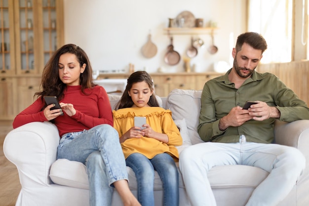 Foto mãe, filha e pai usando smartphone, ignorando um ao outro dentro de casa