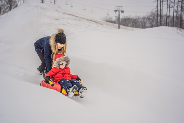 Mãe, filho, passeio em um trenó de inverno inflável diversão de inverno para toda a família