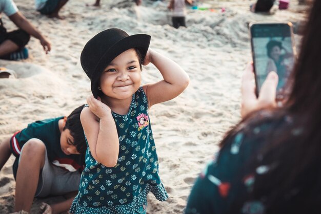 Mãe fotografando filha com celular por um menino na praia