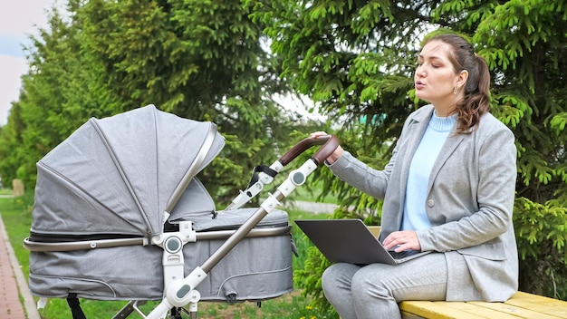 Mãe freelancer trabalha no laptop acalmando bebê no carrinho