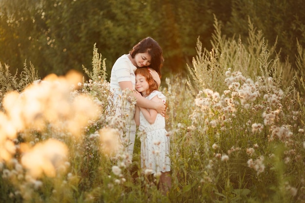 Mãe gentilmente abraça sua filha na natureza em uma noite de verão Cuidados maternos