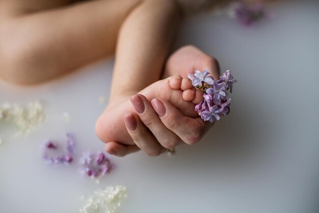 Mãe gentilmente segura o pezinho do bebê no banho floral de leite Mãe tocando a perna do filho