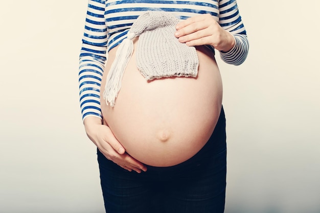 Mãe grávida. Barriga feminina e chapéu de bebê pequeno no fundo