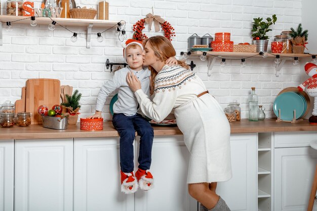 Mãe grávida e seu filho desfrutando na cozinha e na hora do natal. mulher grávida com filho nos feriados de ano novo.