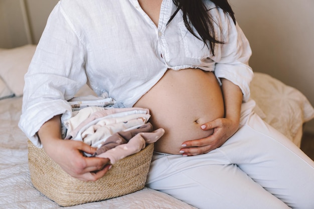 Mãe grávida segura um cesto de roupas de bebê enquanto toca suavemente sua barriga