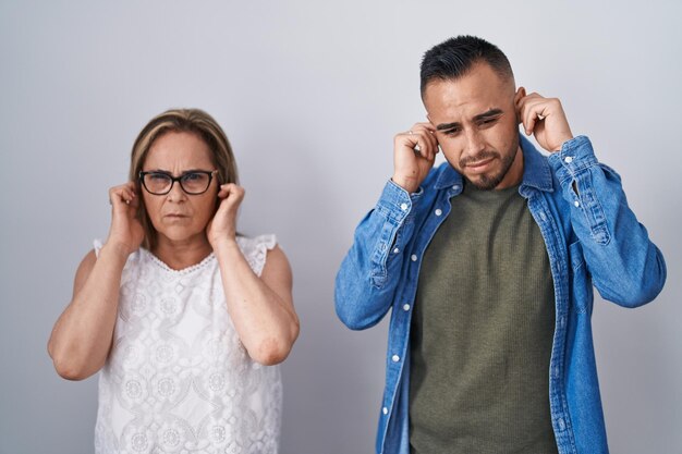 Mãe hispânica e filho juntos cobrindo os ouvidos com os dedos com expressão irritada pelo barulho da música alta. conceito surdo.