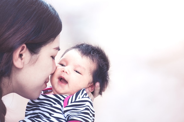 Mãe jovem asiática abraçando e beijando sua menina recém nascida com amor no tom de cor vintage