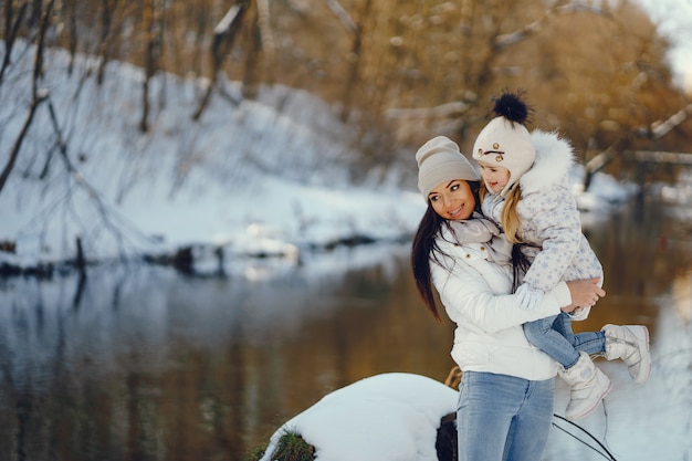 mãe jovem e elegante, brincando com sua filha pouco fofa no parque de neve de inverno