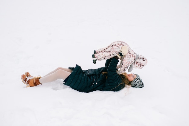 Mãe jovem feliz, brincando com seu bebê adorável no campo de inverno nevado.