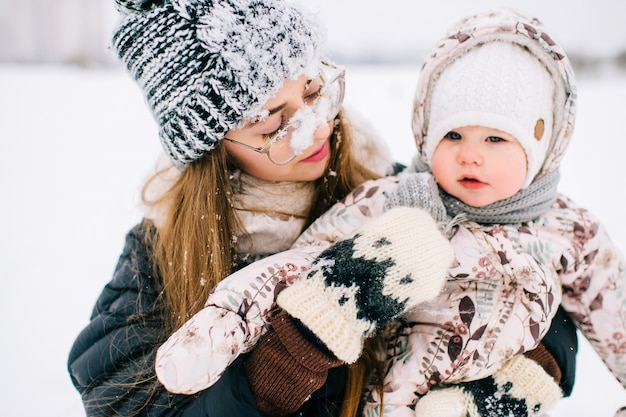 Mãe jovem feliz, brincando com seu bebê adorável no campo de inverno nevado.