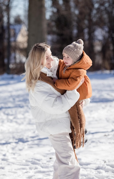 Mãe jovem feliz com filho caminhando no parque de inverno Retrato de família feliz ao ar livre Menino jogando neve na mãe