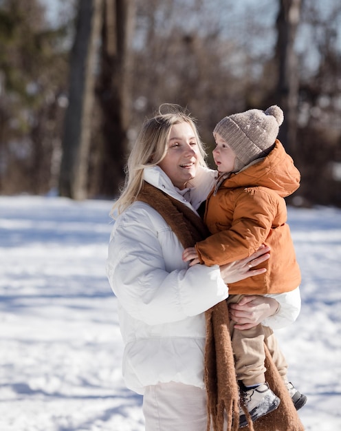 Mãe jovem feliz com filho caminhando no parque de inverno Retrato de família feliz ao ar livre Menino jogando neve na mãe