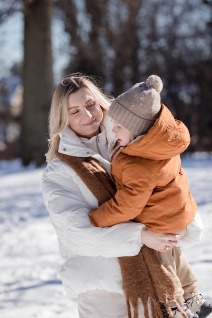 Mãe jovem feliz com filho caminhando no parque de inverno Retrato de família feliz ao ar livre Menino jogando neve na mãe