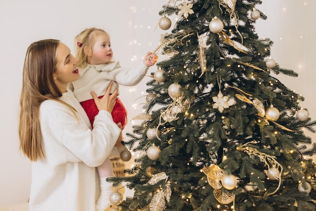 Mãe levantando filha decorando árvore de Natal com ornamentos dourados