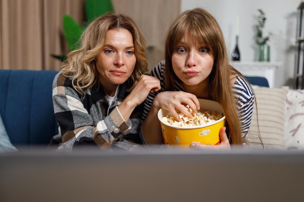 Mãe madura e filha adulta assistindo filme no laptop e comendo pipoca no interior