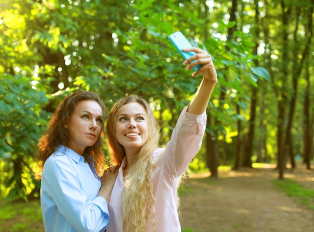 Mãe madura e filha adulta estão fazendo selfie pelo celular no parque de verão