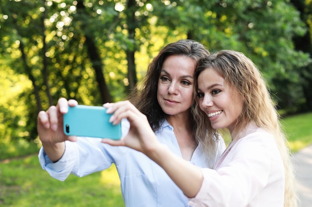 Mãe madura e filha adulta estão fazendo selfie pelo celular no parque de verão