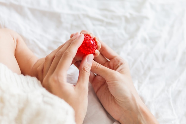 Mãe mantém os pés do bebê recém-nascido. dedos minúsculos e bola de massagem vermelha na mão da mulher.