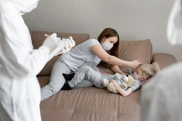 Mãe mede a temperatura do bebê. Médicos em trajes de proteção em pacientes doentes em casa. Coronavírus (COVID-19