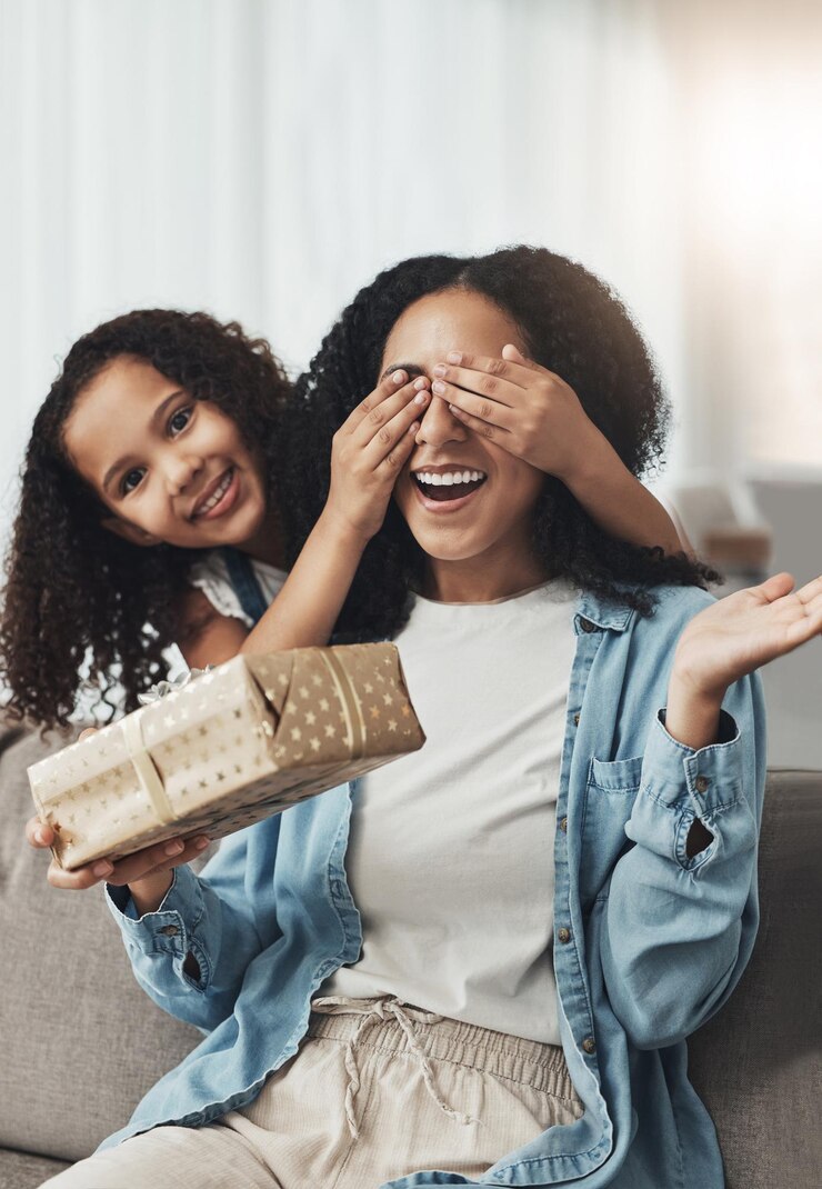 Mãe menina e surpresa com presente no sofá na sala de estar para festa de aniversário ou evento Família amor uau e retrato de criança surpreendendo mamãe feliz com caixa de presente para o dia das mães no sofá em casa