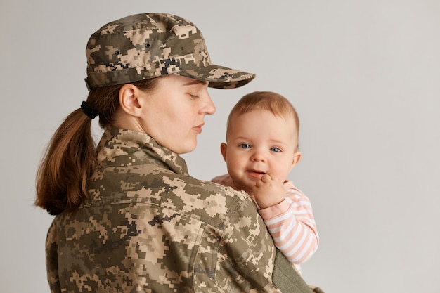 Mãe militar caucasiana vestindo uniforme de camuflagem e chapéu, posando com seu bebê, não via sua filha há muito tempo, sentindo falta de seu filho enquanto servia no exército.