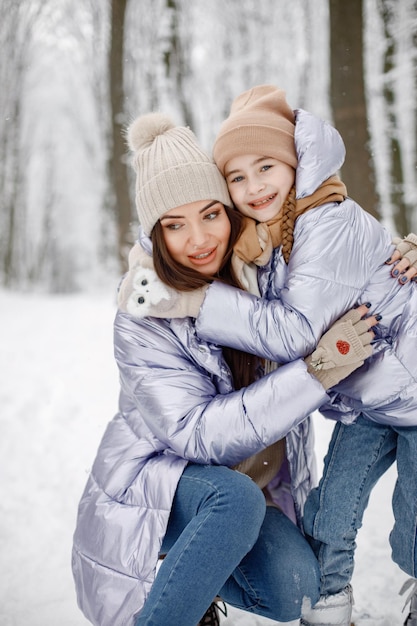 Mãe morena e sua filha em pé na floresta de inverno