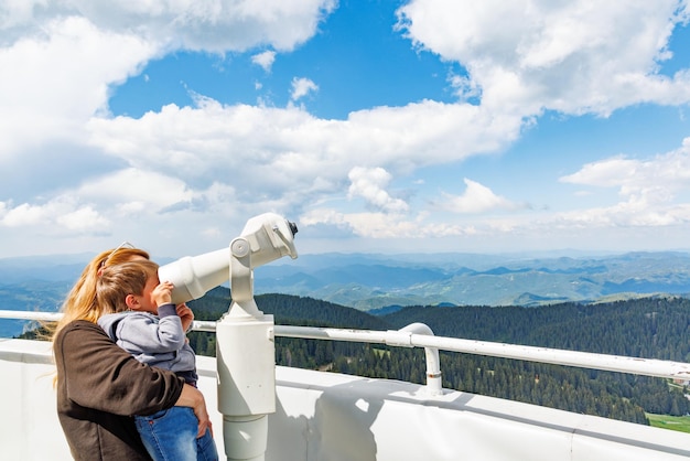 Mãe mostra paisagens de filho no vale das montanhas Rhodope e céu através do telescópio na torre de observação de Snezhan