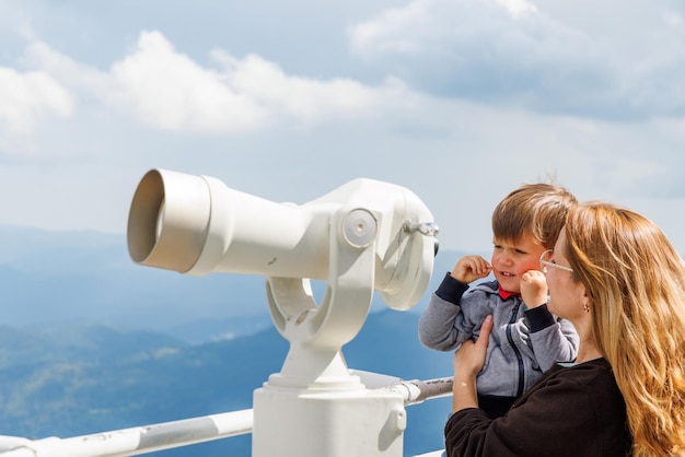 Mãe mostra paisagens de filho no vale das montanhas rhodope e céu através do telescópio na torre de observação de snezhan