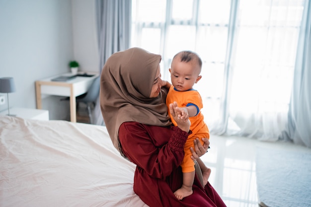 Mãe muçulmana asiática, segurando seu filho no colo, jogando juntos