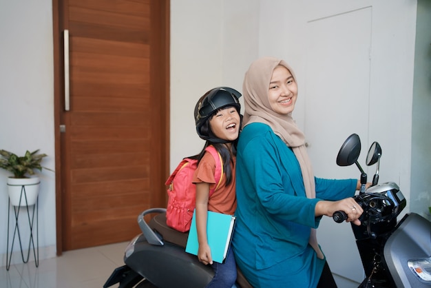 Mãe muçulmana levando a filha para a escola de moto pela manhã