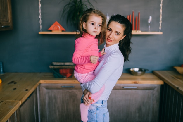 Mãe muito jovem, segurando sua filha nas mãos na cozinha