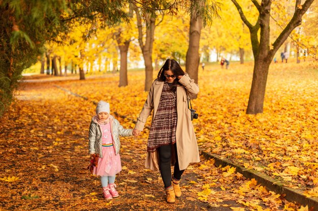 Mãe mulher com filha bebê caminhando no parque de outono com folhagem amarela