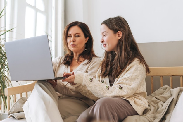 Mãe mulher de meia idade e filha adolescente usando laptop juntos no interior da luz