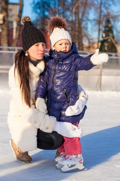 Mãe nova e sua filha pequena bonito em uma pista de patinagem