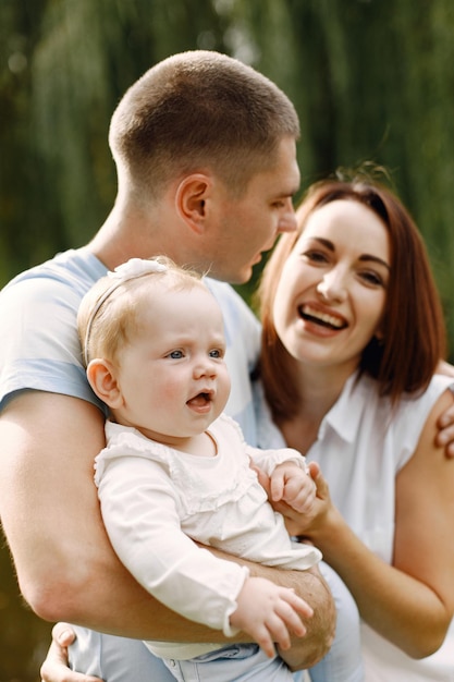 Mãe, pai e filha bebê em pé no parque e posando para uma foto. família vestindo roupas brancas e azuis claras